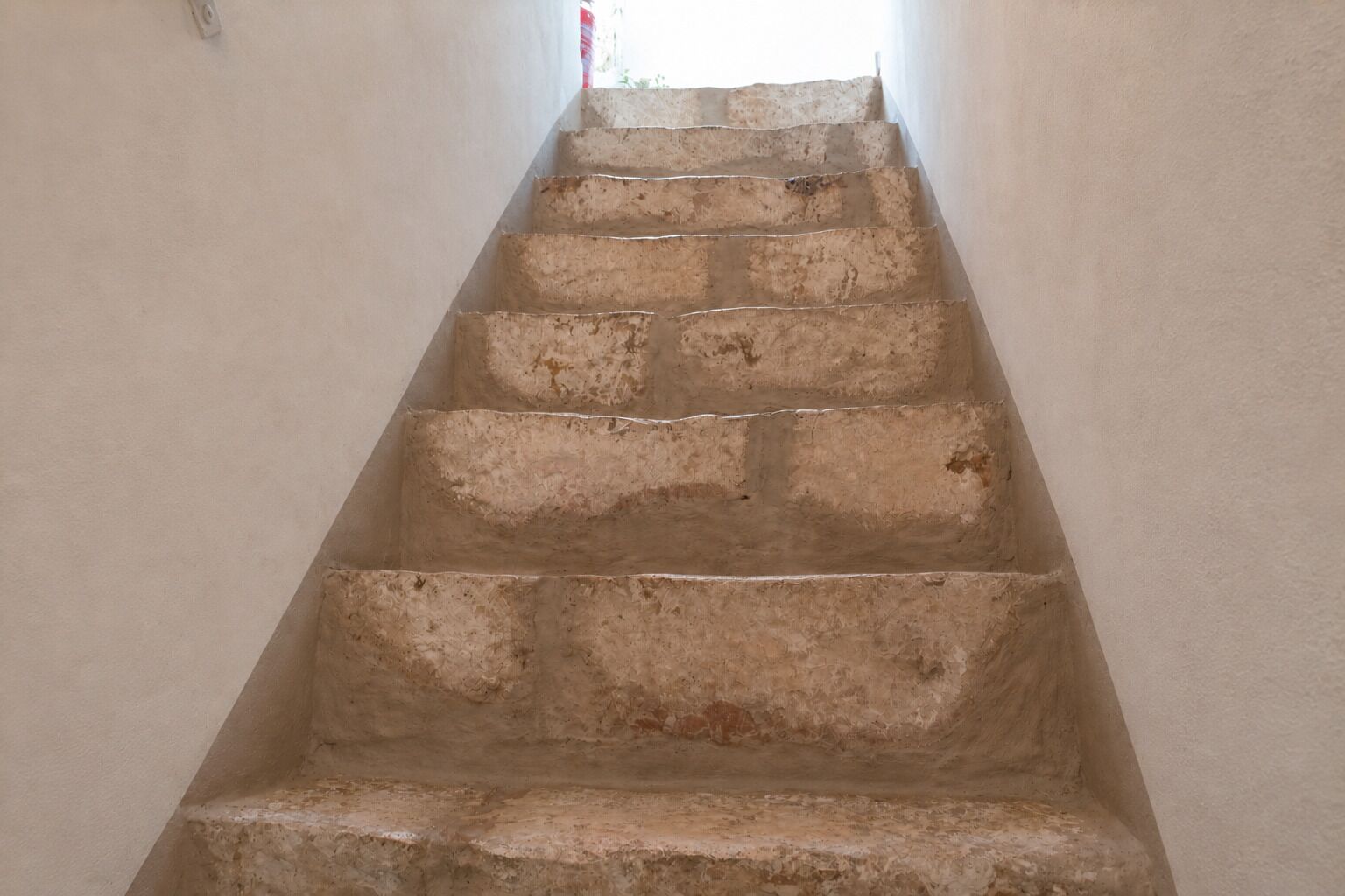 A staircase with a textured wall on either side, leading upwards.