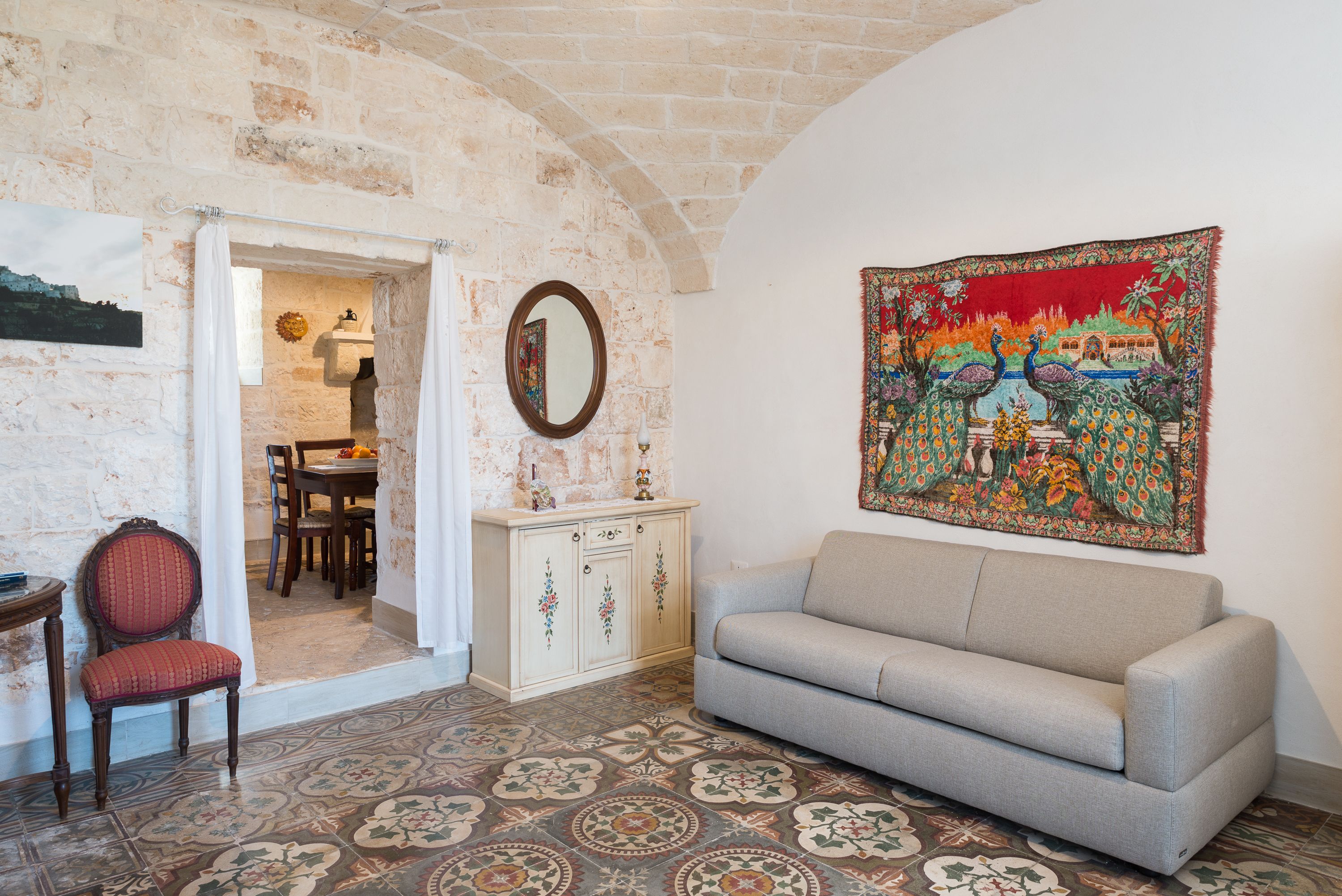 A room with a patterned floor, a sofa, a chair, a cabinet, and a wall tapestry.