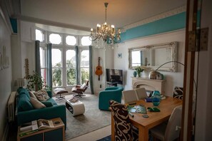 A living room with a sofa, chairs, a dining table, a TV, and a guitar. - Sea View Ultimate Boutique Escape! (Ilfracombe)
