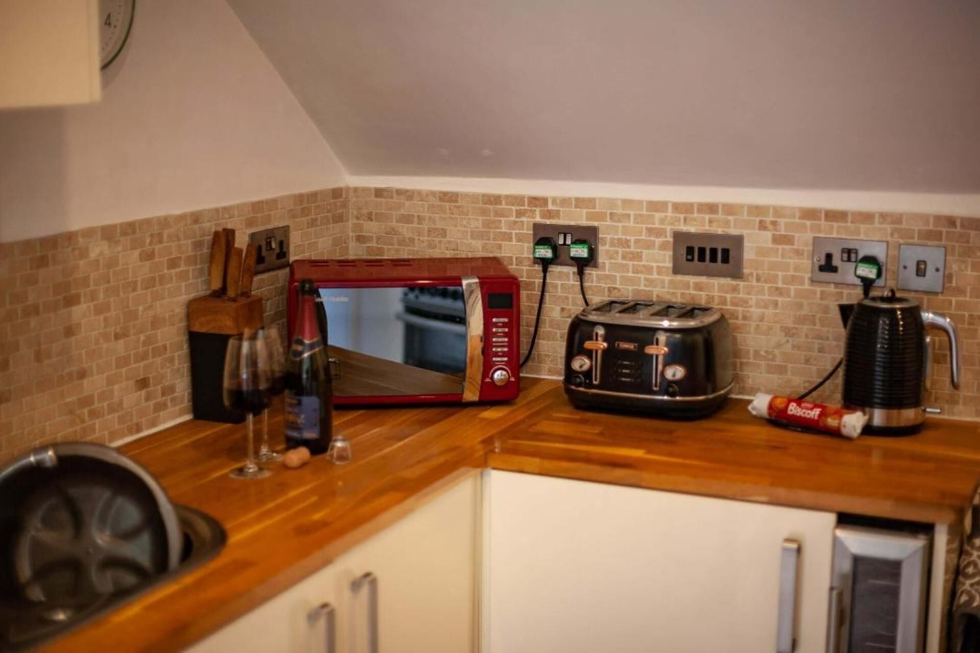 A kitchen with a brick backsplash, a red toaster oven, a black toaster, and a coffee maker.