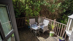 Een houten terras met rieten stoelen en een kleine tafel, omringd door weelderige beplanting.