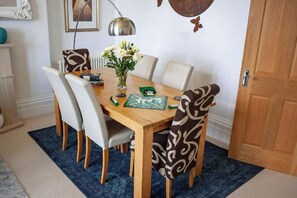 A dining area with a wooden table, white chairs, a vase with flowers, and a board game.