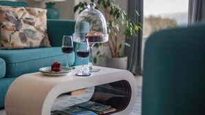 Een moderne woonkamer met een blauwgroene bank, een glazen salontafel met dessert- en wijnglazen, en uitzicht door een raam.