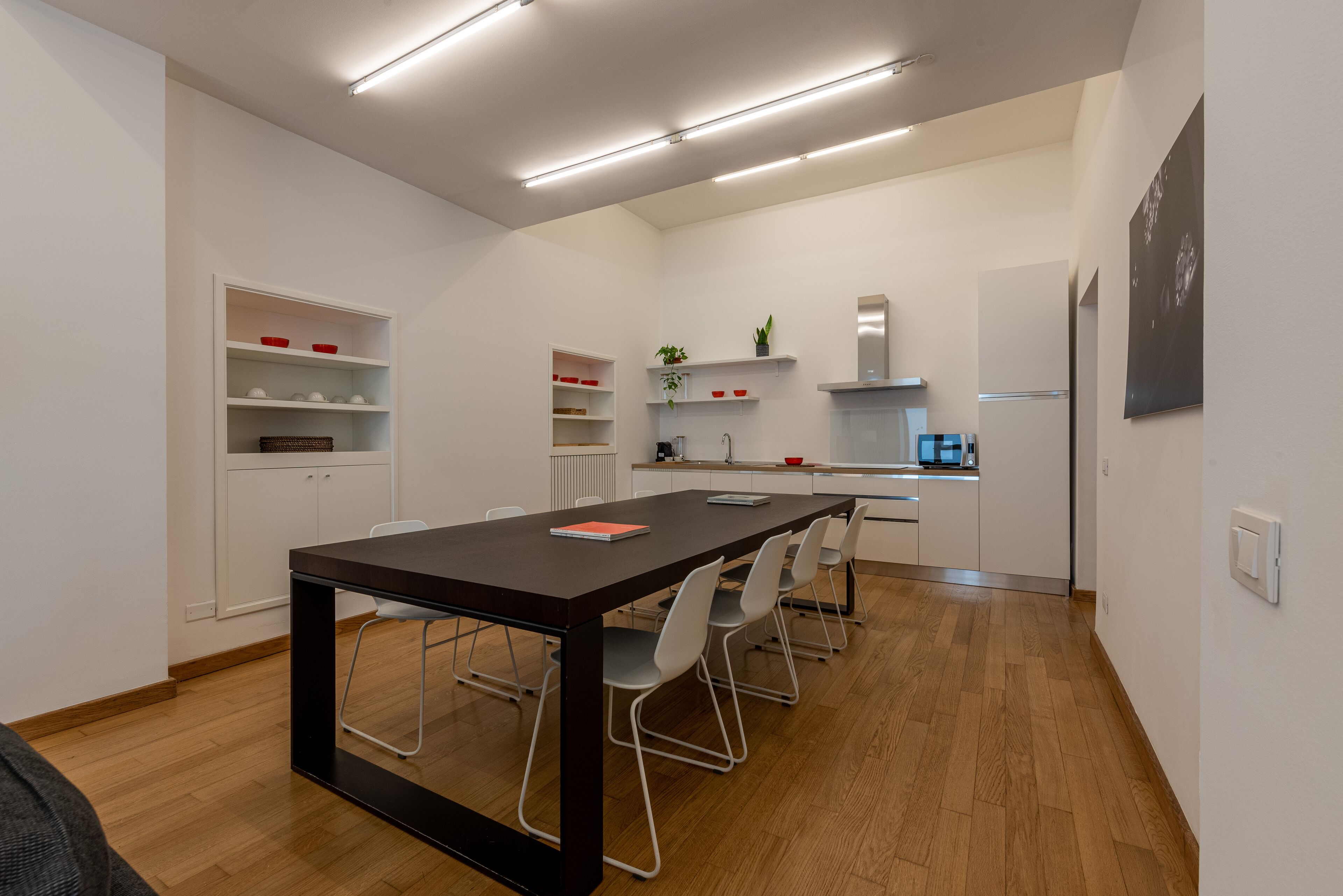 A modern kitchen with white cabinets, a wooden dining table, and a built-in oven.
