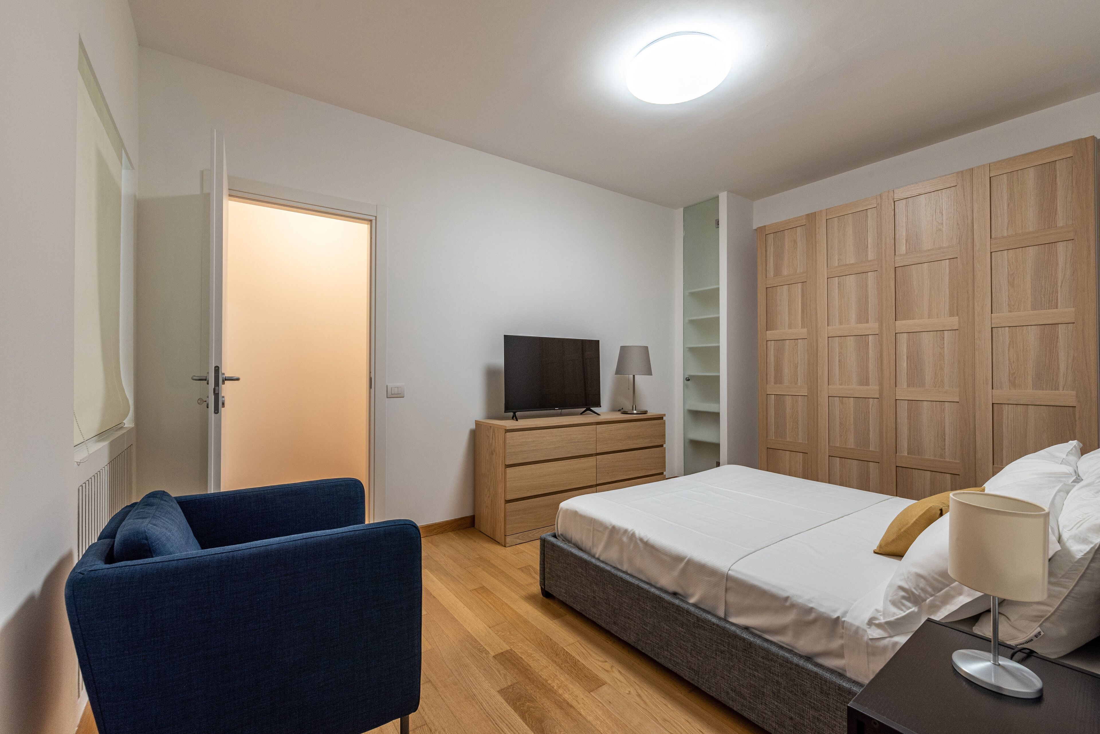 Een slaapkamer met een bed, een televisie op een dressoir, een stoel en een kledingkast.