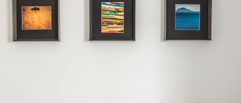 A room with a beige sofa, three framed artworks on the wall, and two black cushions.
