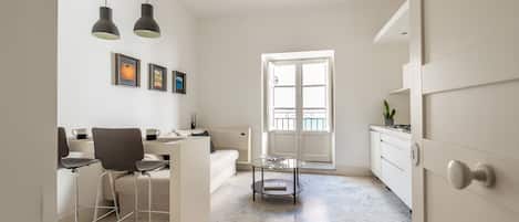 A modern, minimalist living space with a dining area, a sofa, a coffee table, and a view through a large window.