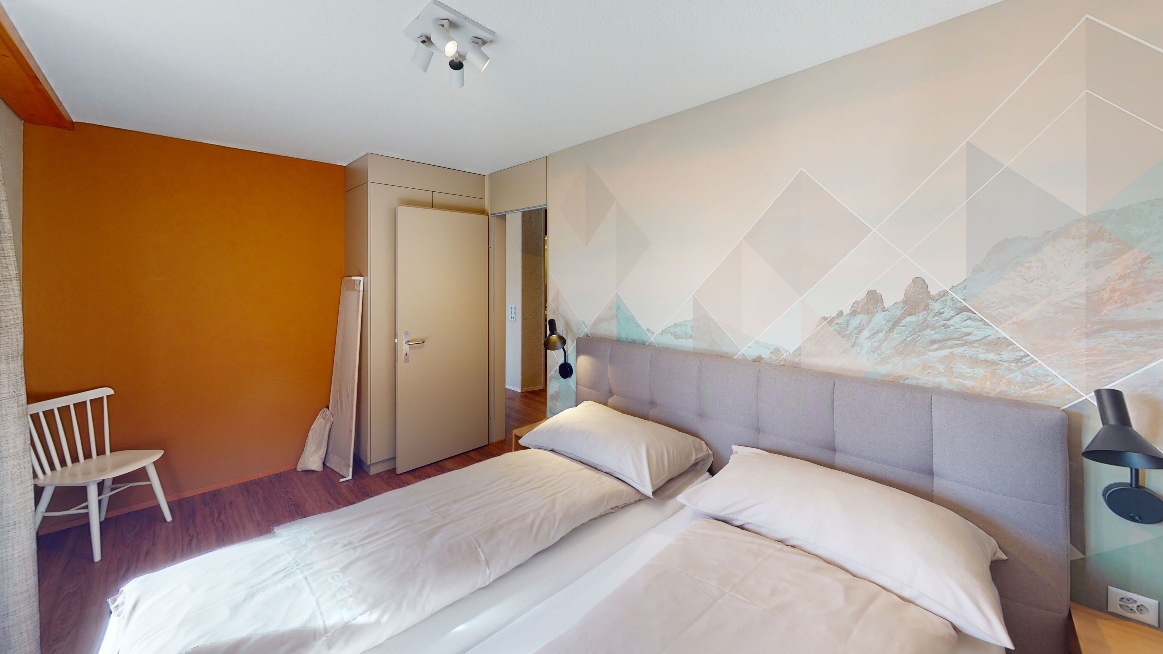 A bedroom with a bed, a chair, a door, and a wall with a mountain painting.
