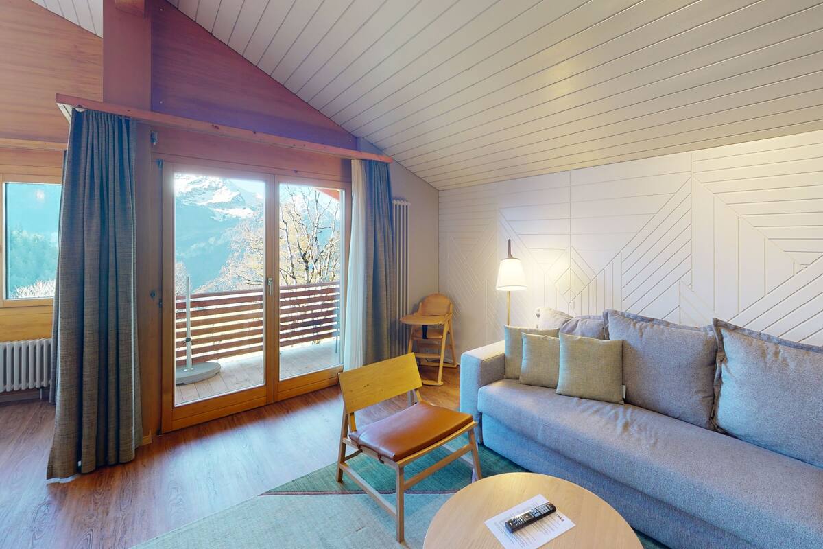 A modern living room with a sofa, a wooden chair, a lamp, and a view through a sliding glass door.