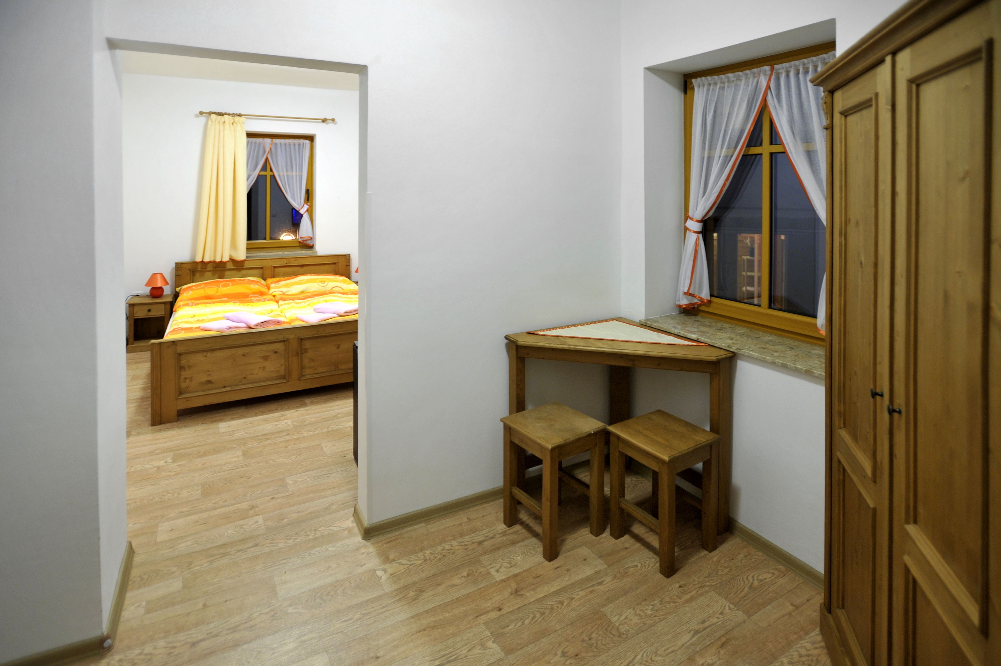 A bedroom with a wooden bed, a desk with two chairs, and a window with curtains.