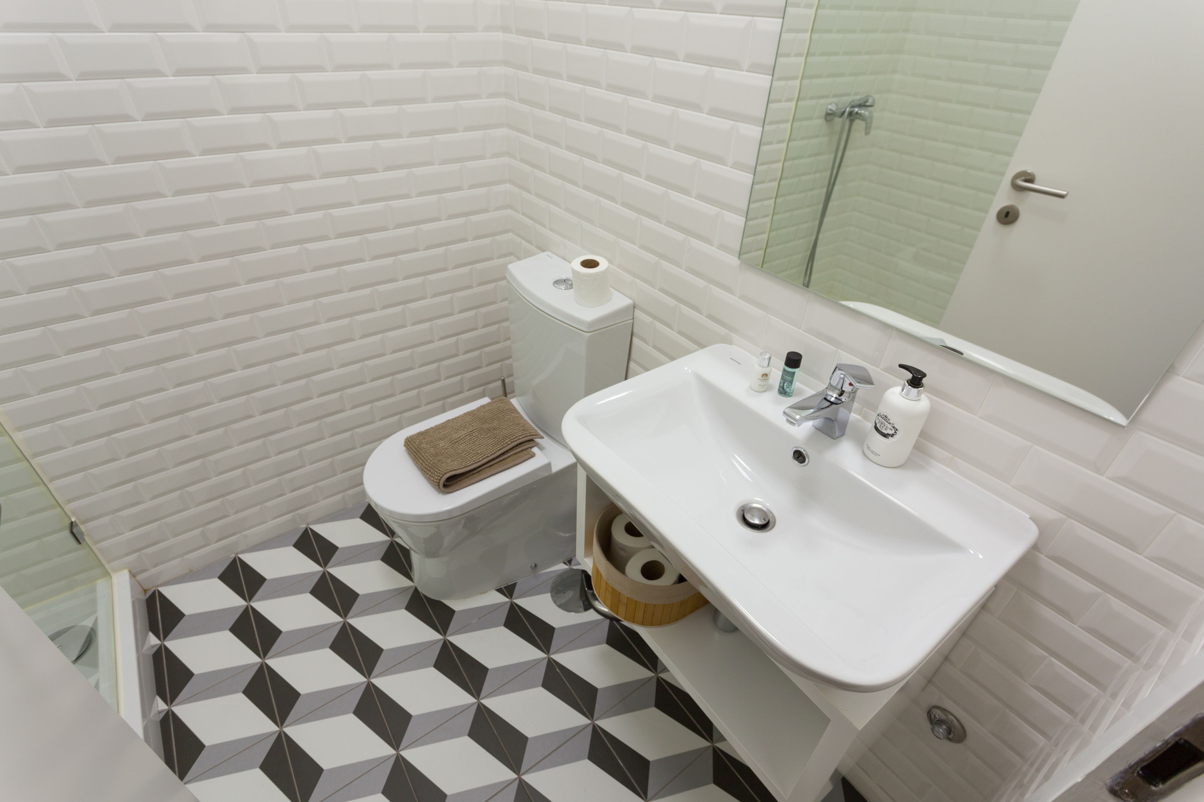 A bathroom with a white toilet, a sink with a mirror, and a patterned floor.
