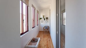 Un pasillo estrecho con suelo de madera, una silla de mimbre y una pequeña mesa con una bandeja.