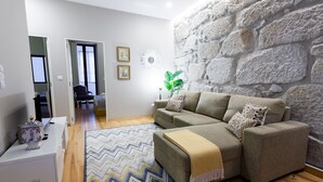 Una sala de estar moderna con una pared de piedra, un sofá gris, un tapiz estampado y una mesita con un adorno.