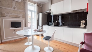 Una cocina moderna con armarios blancos, un salpicadero de azulejos negros, un refrigerador de acero inoxidable y un microondas. Hay una zona de comedor con una mesa blanca y dos sillas.