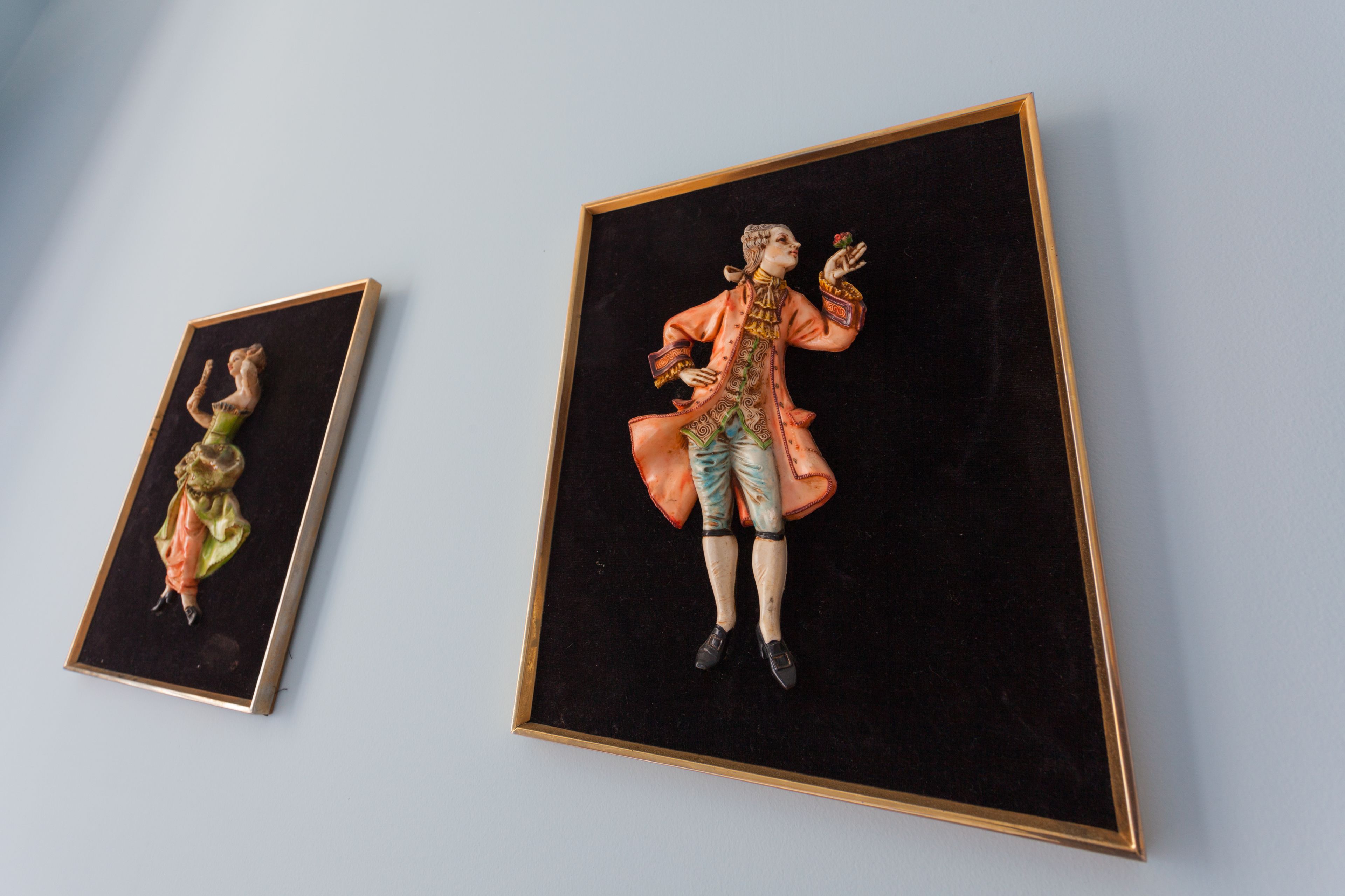 Two framed porcelain figurines on a wall.