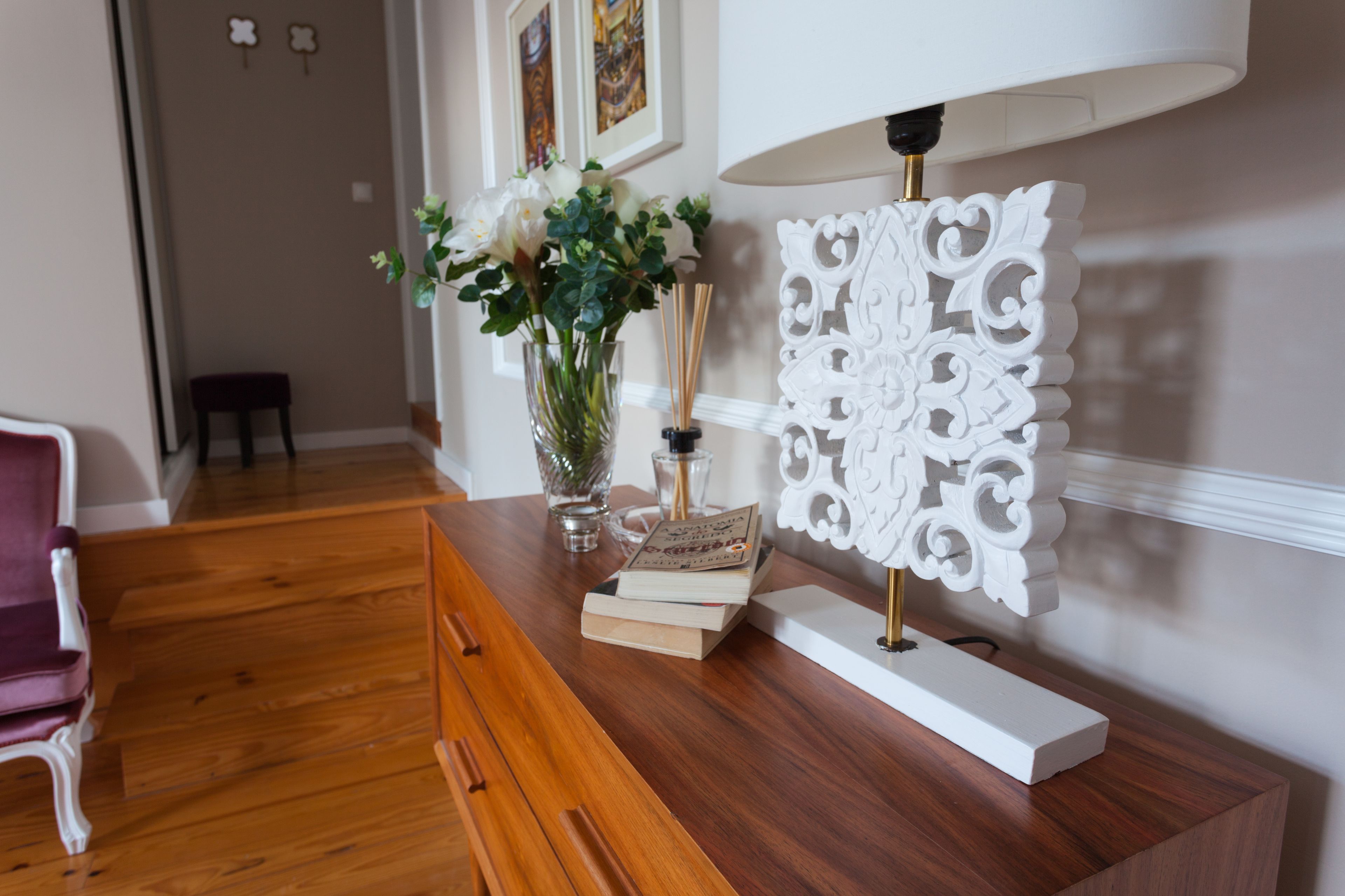 A wooden desk with a white decorative lamp, a vase with flowers, and a book.