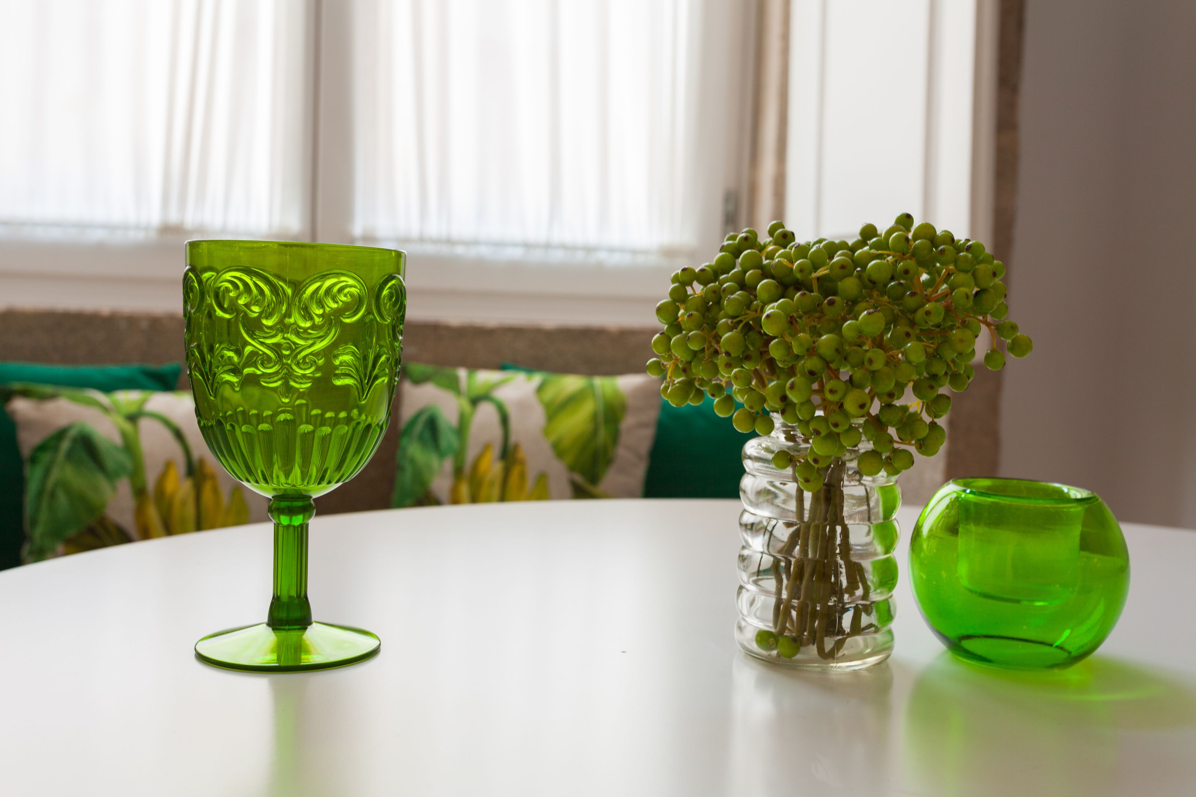 Una mesa redonda con un florero verde de vidrio que contiene uvas verdes y otro florero de vidrio transparente con vidrio verde.