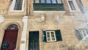 Un edificio histórico con entrada central, varias ventanas con contraventanas y una puerta decorativa.