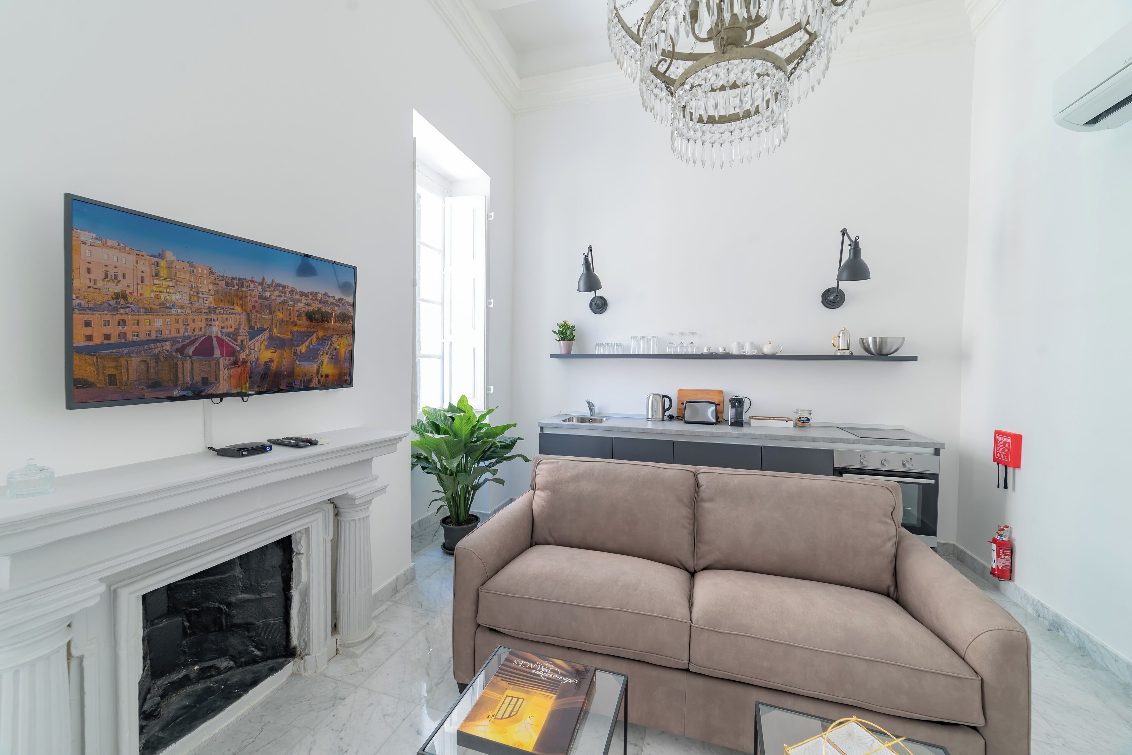 A living room with a beige sofa, a fireplace, a TV mounted on the wall, and a chandelier.