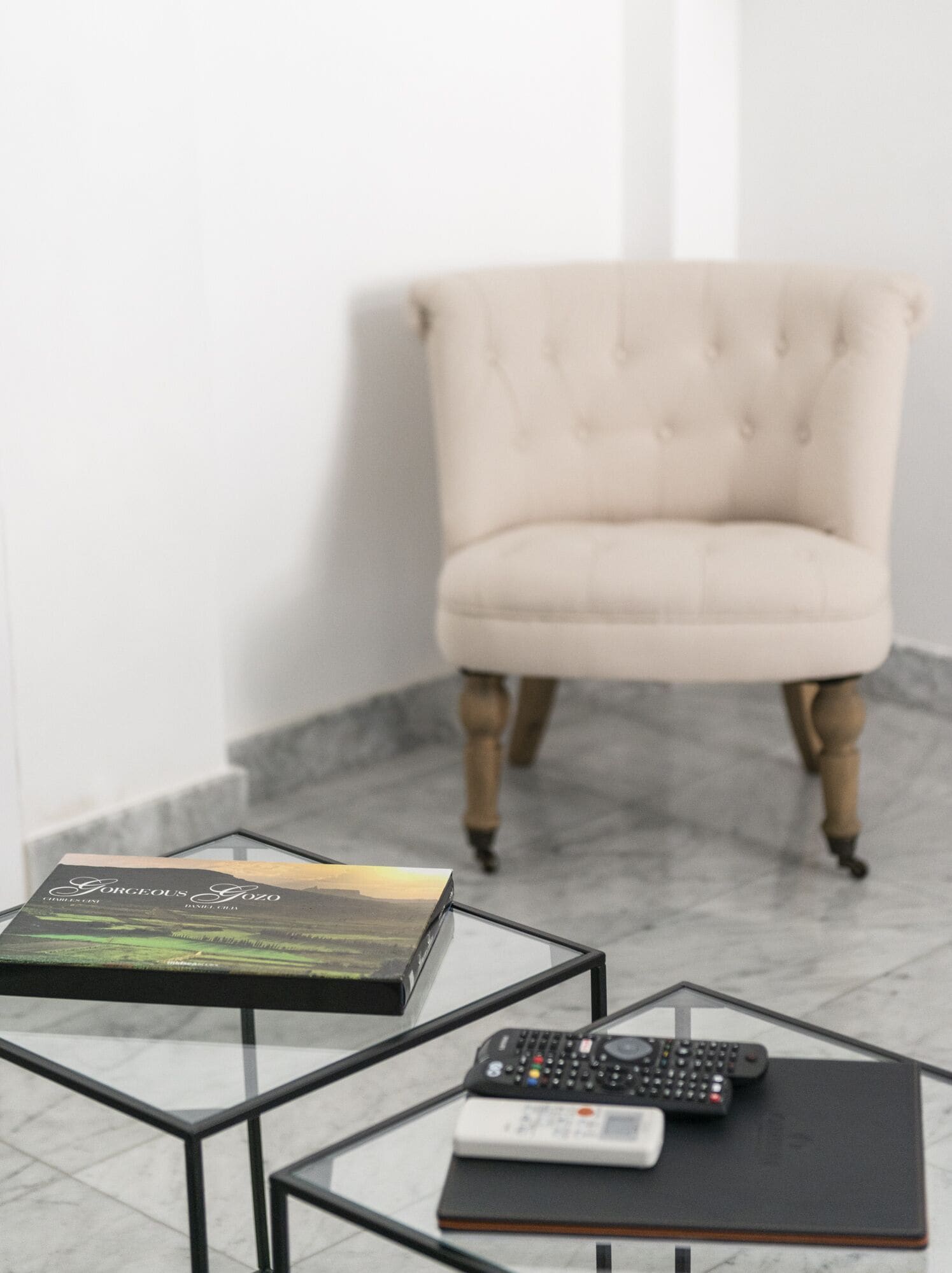 Une chaise, une table avec un livre et une télécommande, et un sol en marbre.