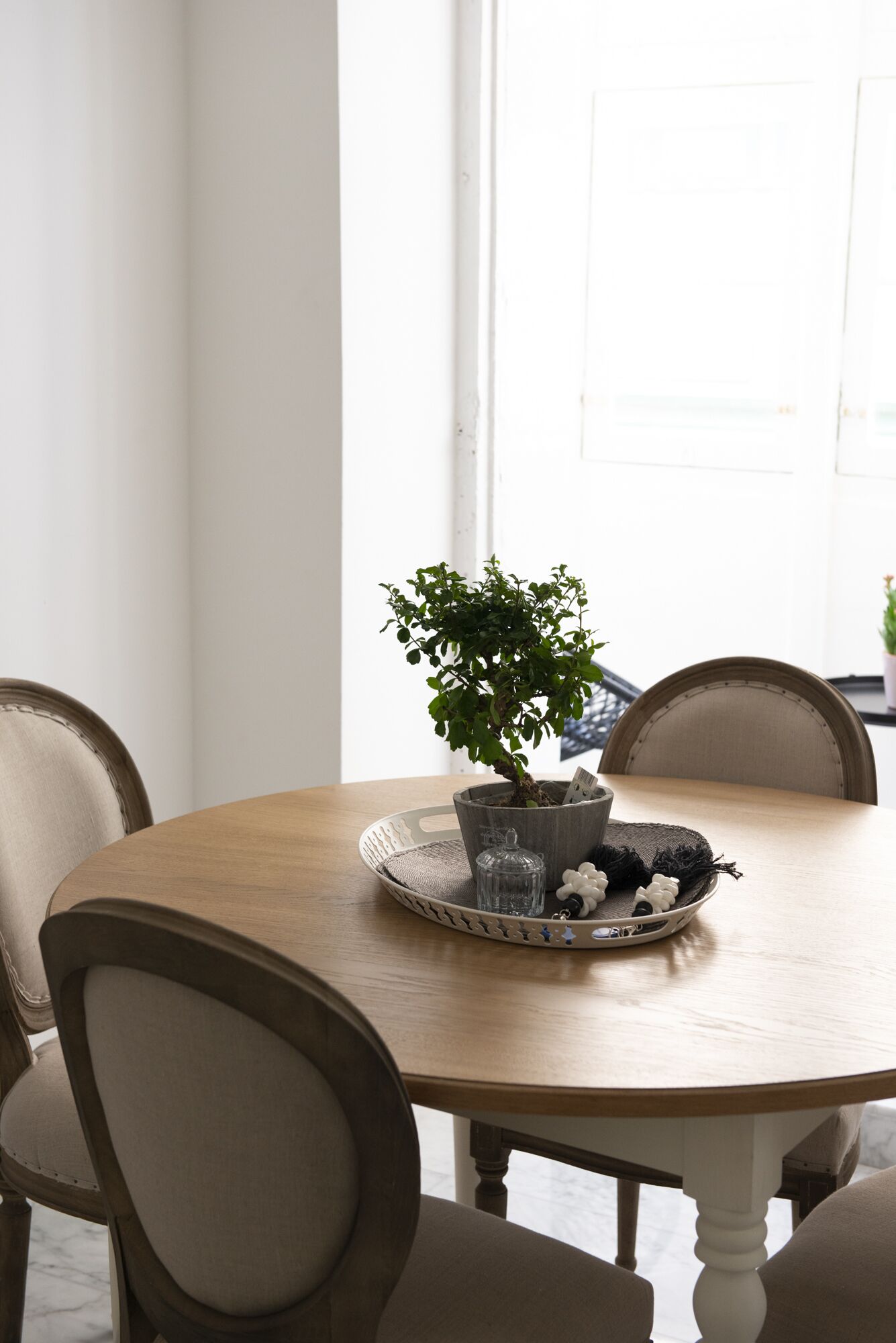 A round wooden dining table with a potted plant and a decorative tray.