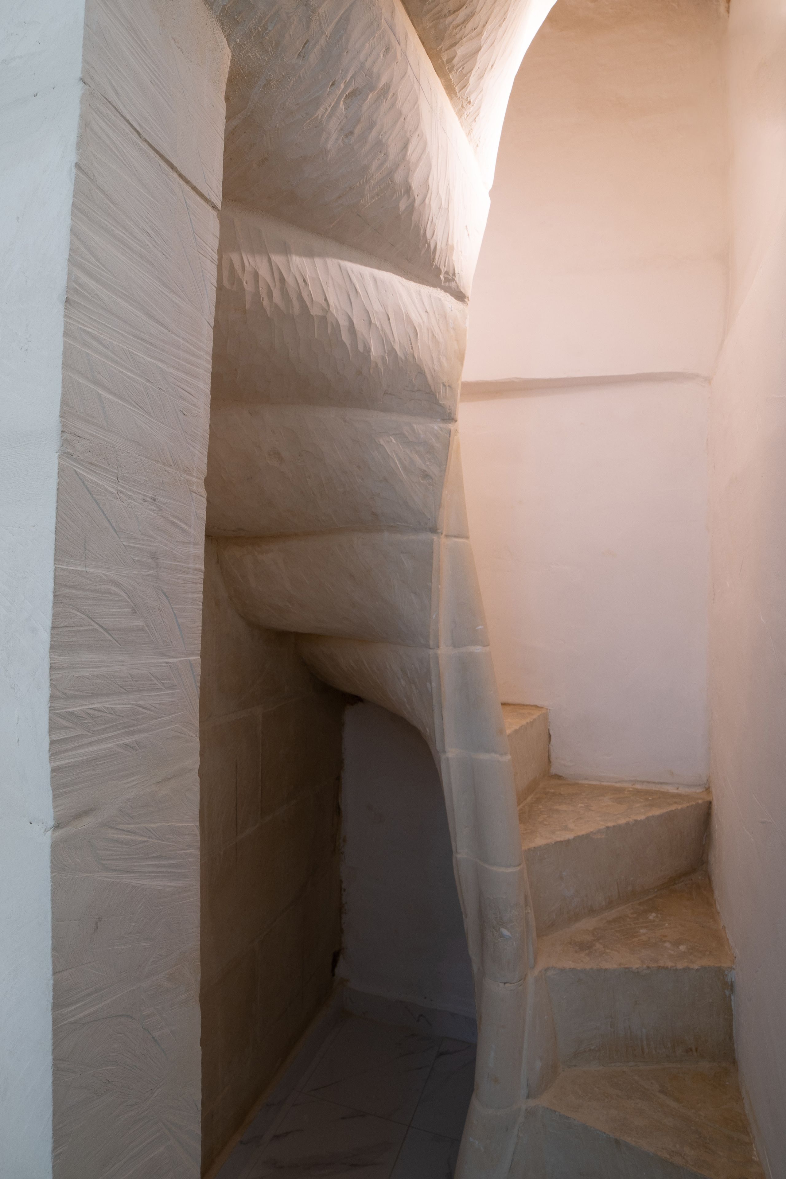 Una estrecha escalera de piedra, con un muro curvo a un lado y otro recto al otro, que lleva a una plataforma.