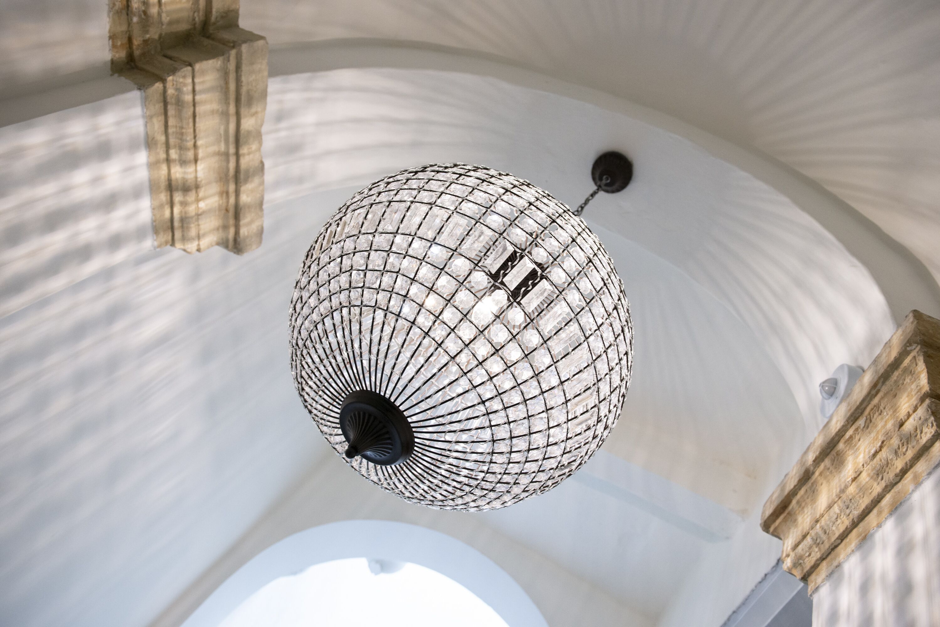 A spherical chandelier with a grid pattern, hanging from a ceiling with a curved design.
