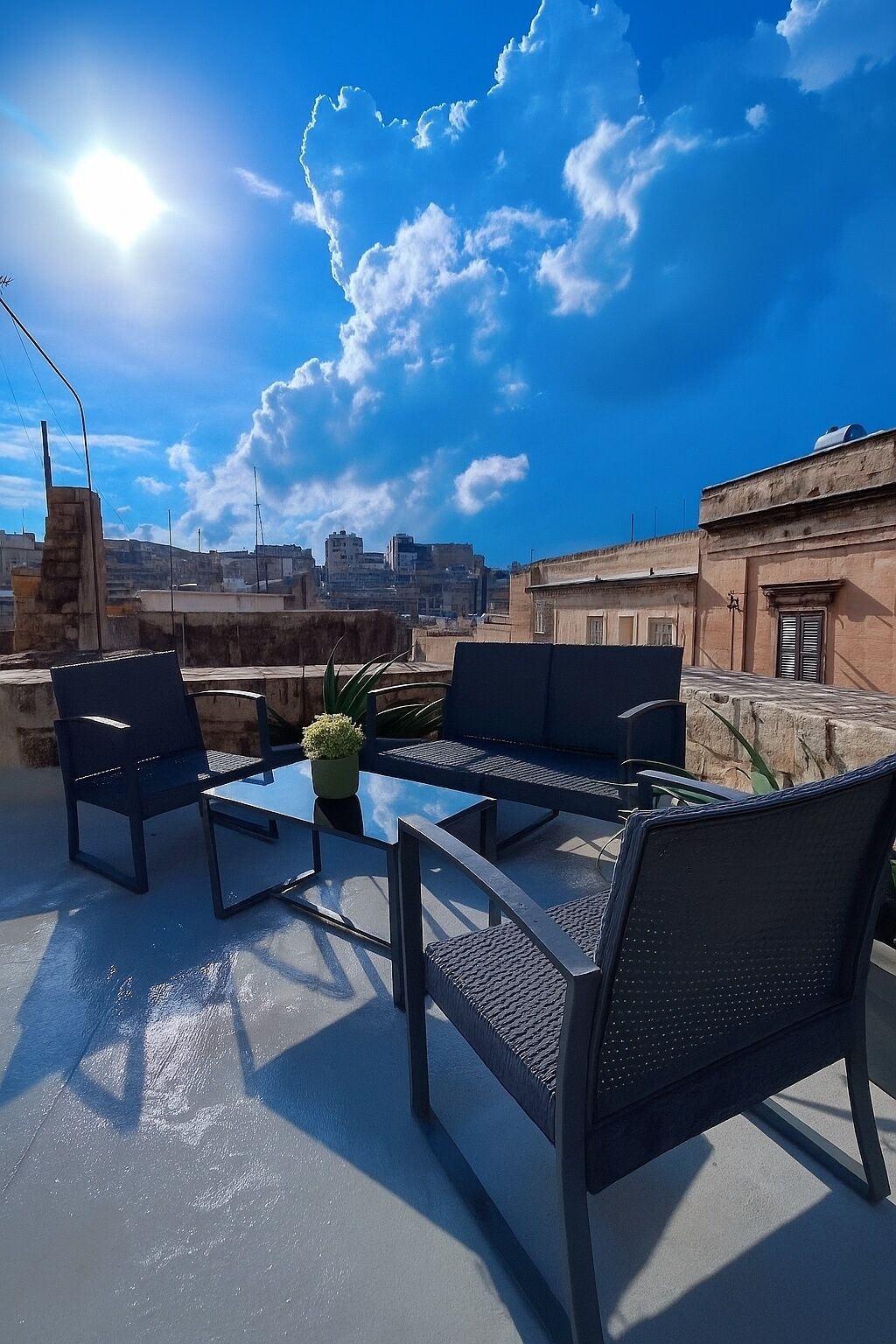 Une terrasse sur le toit, aménagée avec du mobilier d’extérieur, une table en verre et un pot de fleurs.