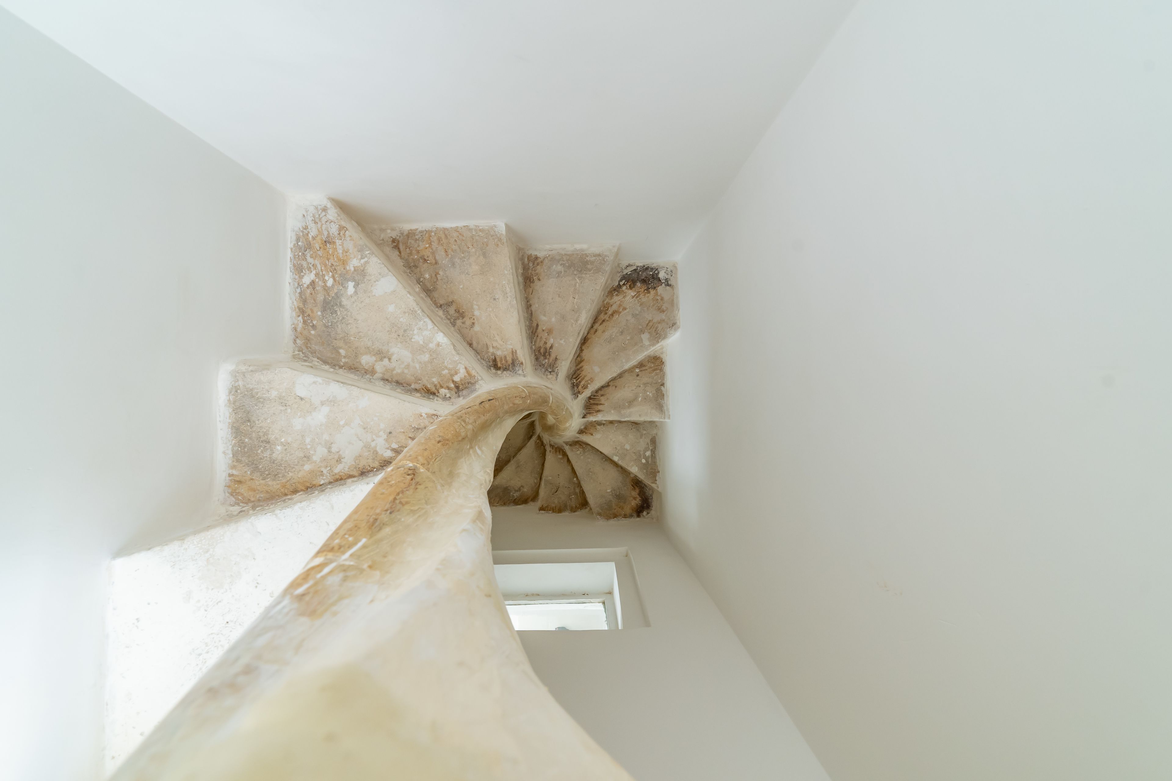 Uma escada em espiral com textura rústica e inacabada, que leva a uma pequena janela no topo.
