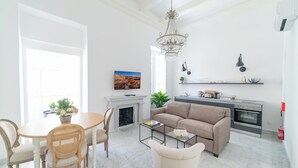 Una sala de estar moderna con chimenea, un sofá, una mesa de comedor con sillas y una zona de cocina con encimera y electrodomésticos.
