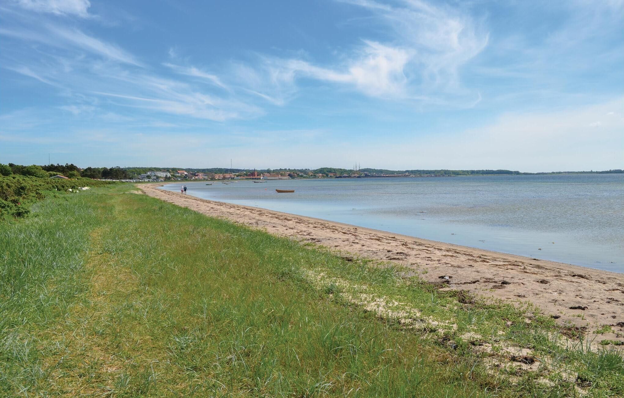 Ein Strand mit sandigem Ufer, ruhigem Wasser und einer entfernten Ansicht einer Stadt.