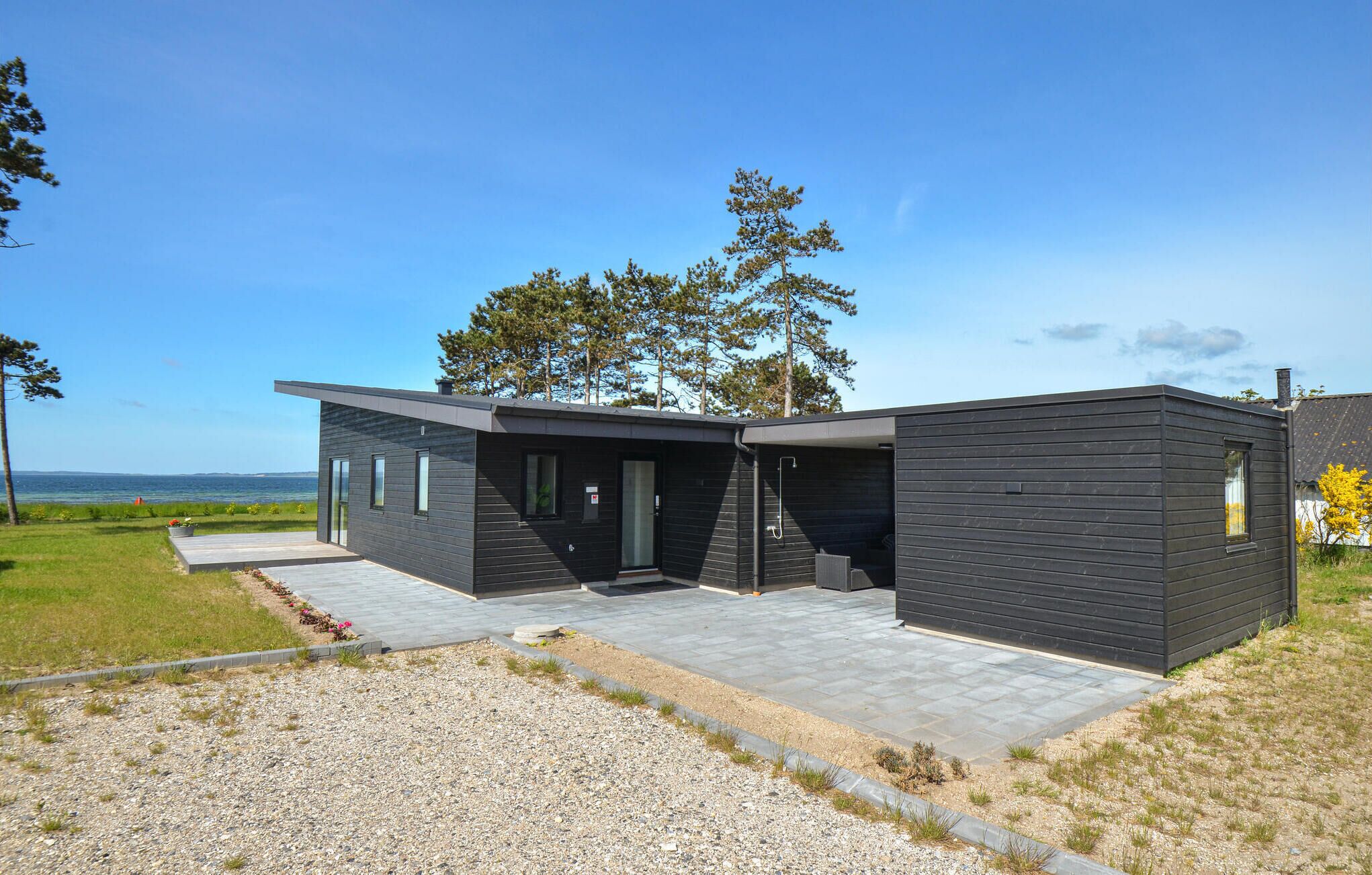 A modern two-story house with a dark exterior, a covered patio, and a view of the sea.