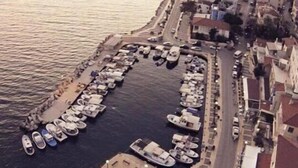 An aerial view of a marina with boats docked along a waterfront, surrounded by buildings and a road. - Ufuk Hotel (Çeşme)