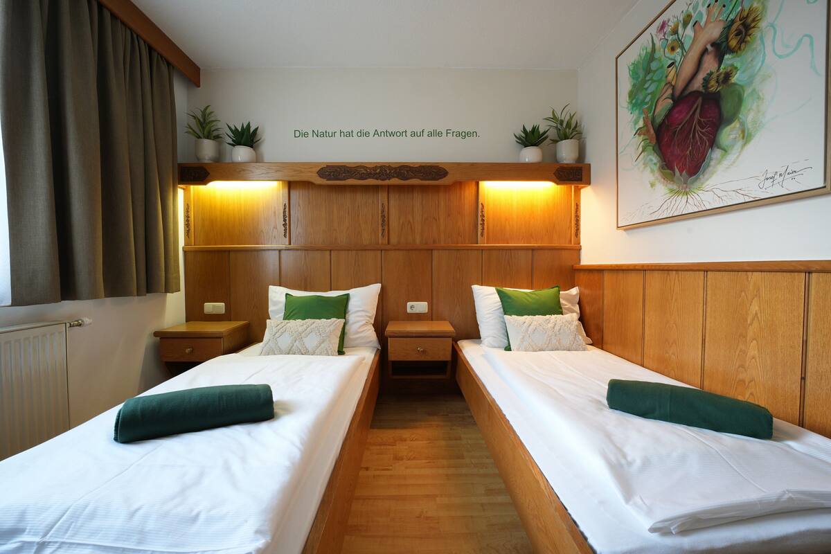 A hotel room with two beds, wooden headboard, bedside tables, lamps, and a wall-mounted artwork.