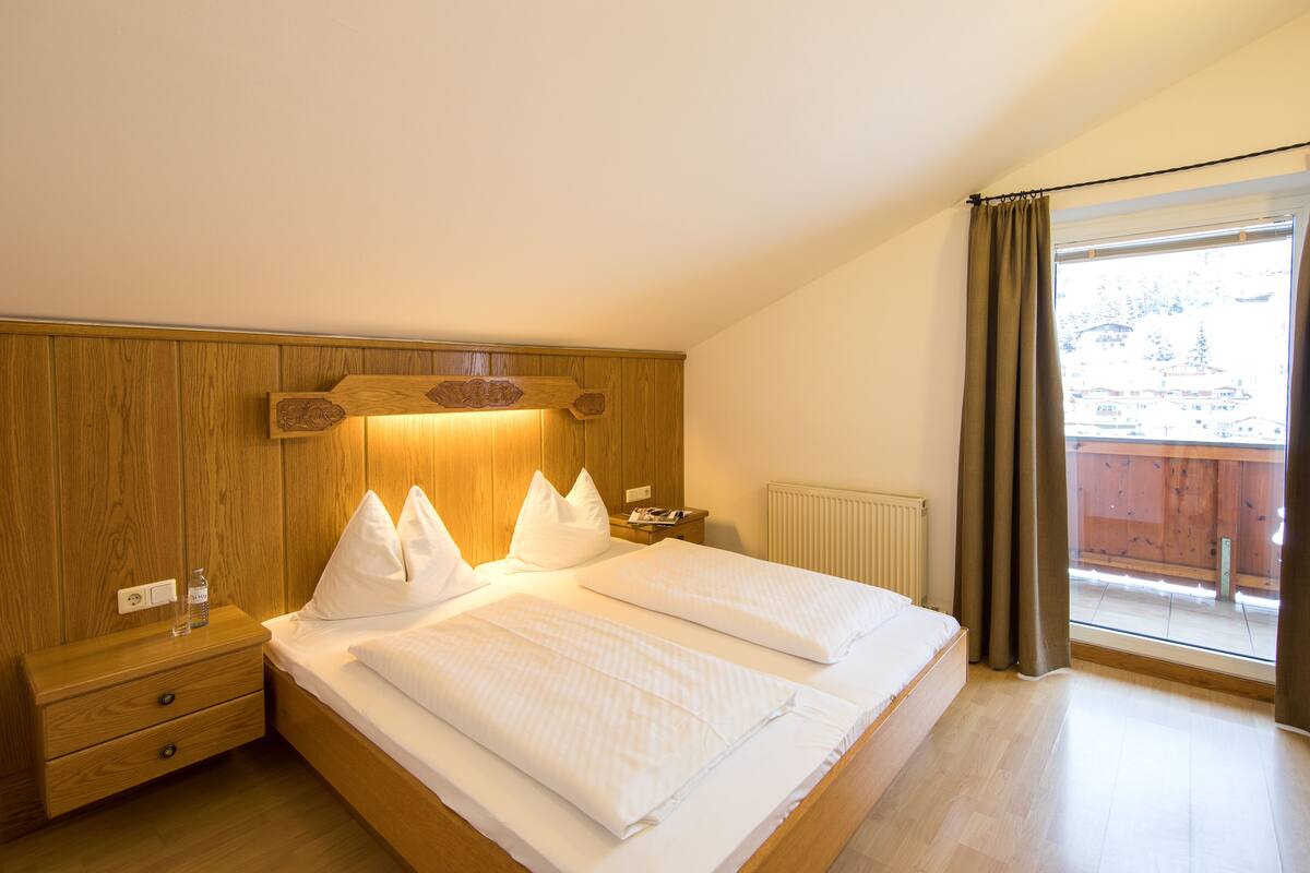 A bedroom with a wooden headboard, a large bed with white bedding, a nightstand, and a window with curtains.
