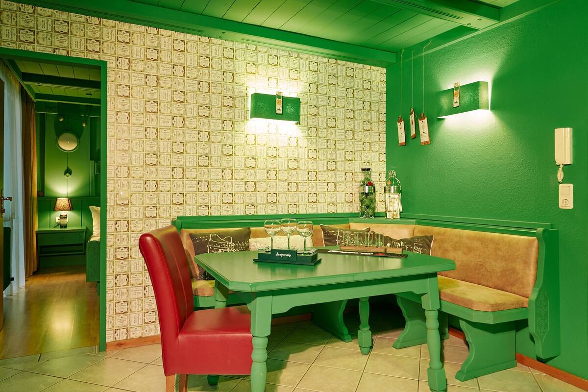 A room with a green wall, a patterned wallpaper, a green table, and a red chair.