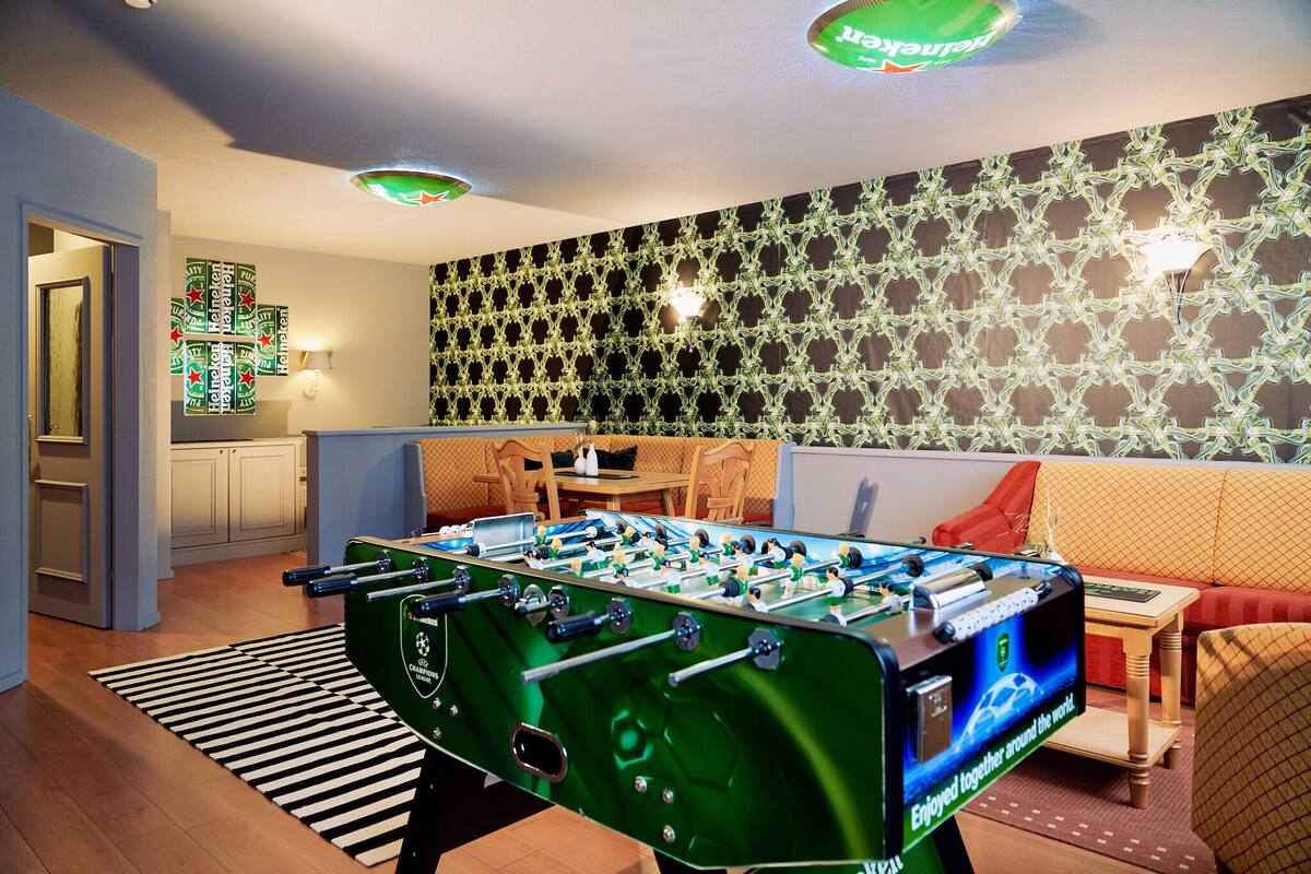 A room with a foosball table, a kitchen area, and a patterned wall.