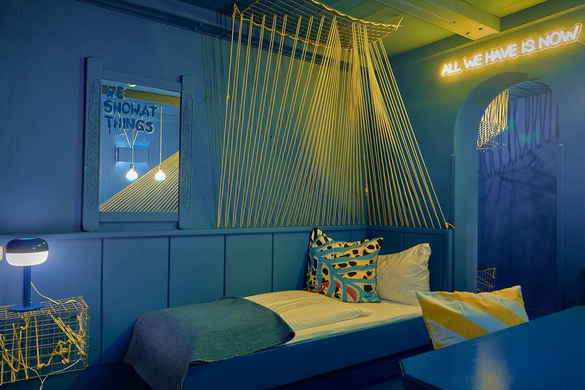 A bedroom with a bed, a bedside table, a lamp, and a wall with a neon sign.