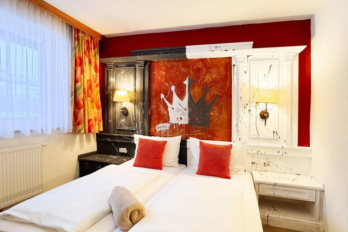 A hotel room with a large bed, red and white walls, a decorative tapestry, and a white dresser.