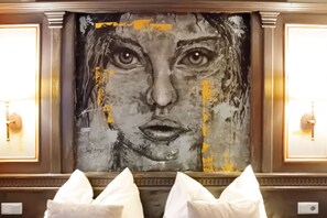 A framed artwork with a textured surface and visible yellow markings, flanked by two wall-mounted light fixtures.