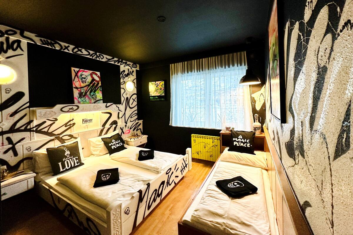 A room with two beds, graffiti on the walls, and a window with curtains.