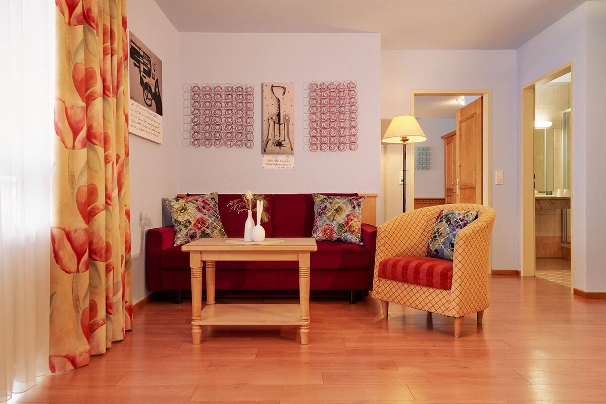 A living room with a wooden floor, a red sofa, a wooden coffee table, and a patterned armchair.
