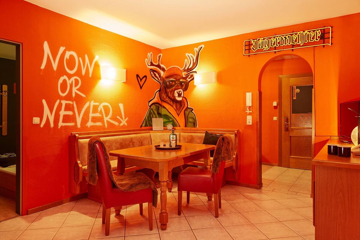 A restaurant with a vibrant orange interior, a wooden table with chairs, and a wall mural of a deer.