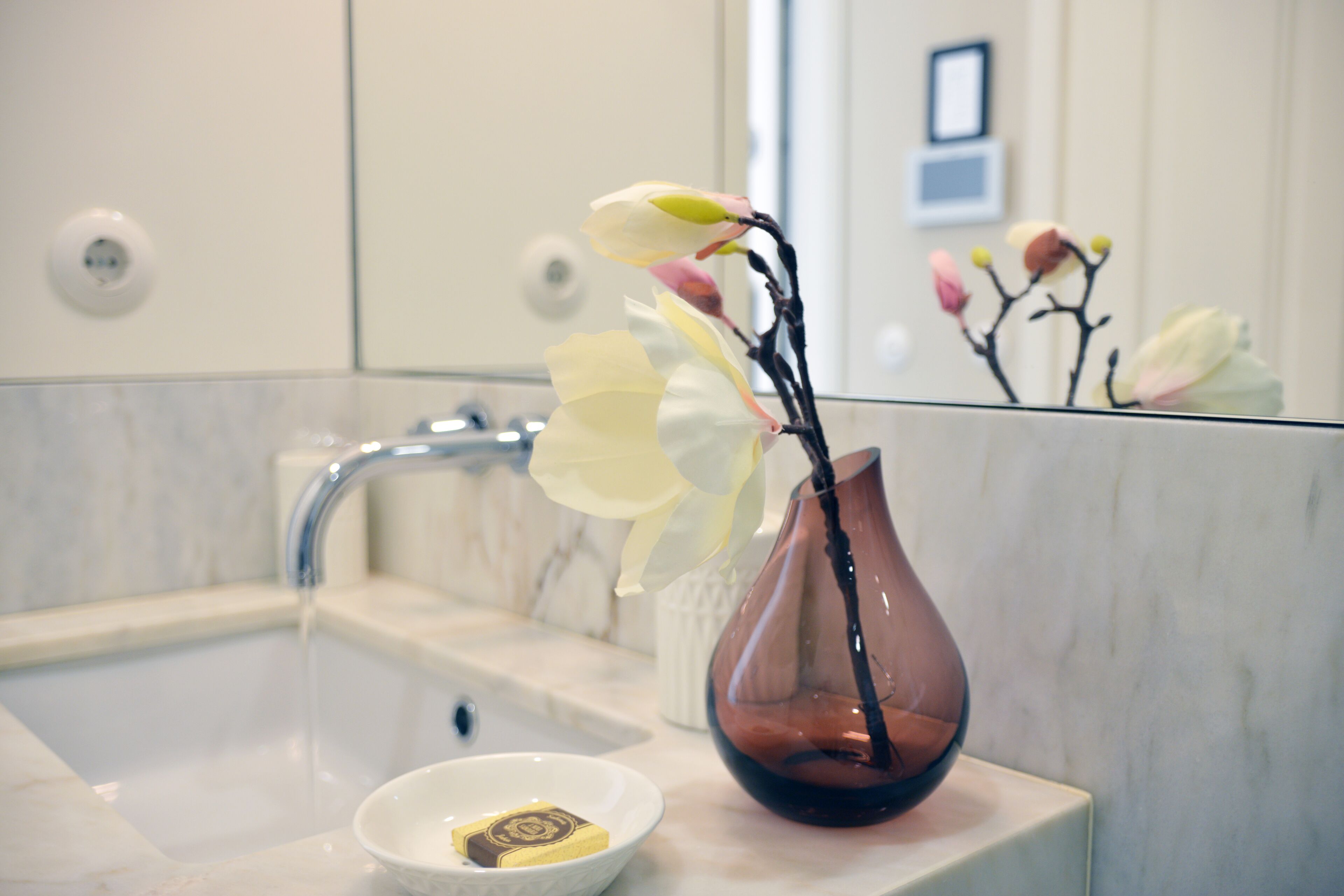 A bathroom sink with a vase of flowers and a soap dish.