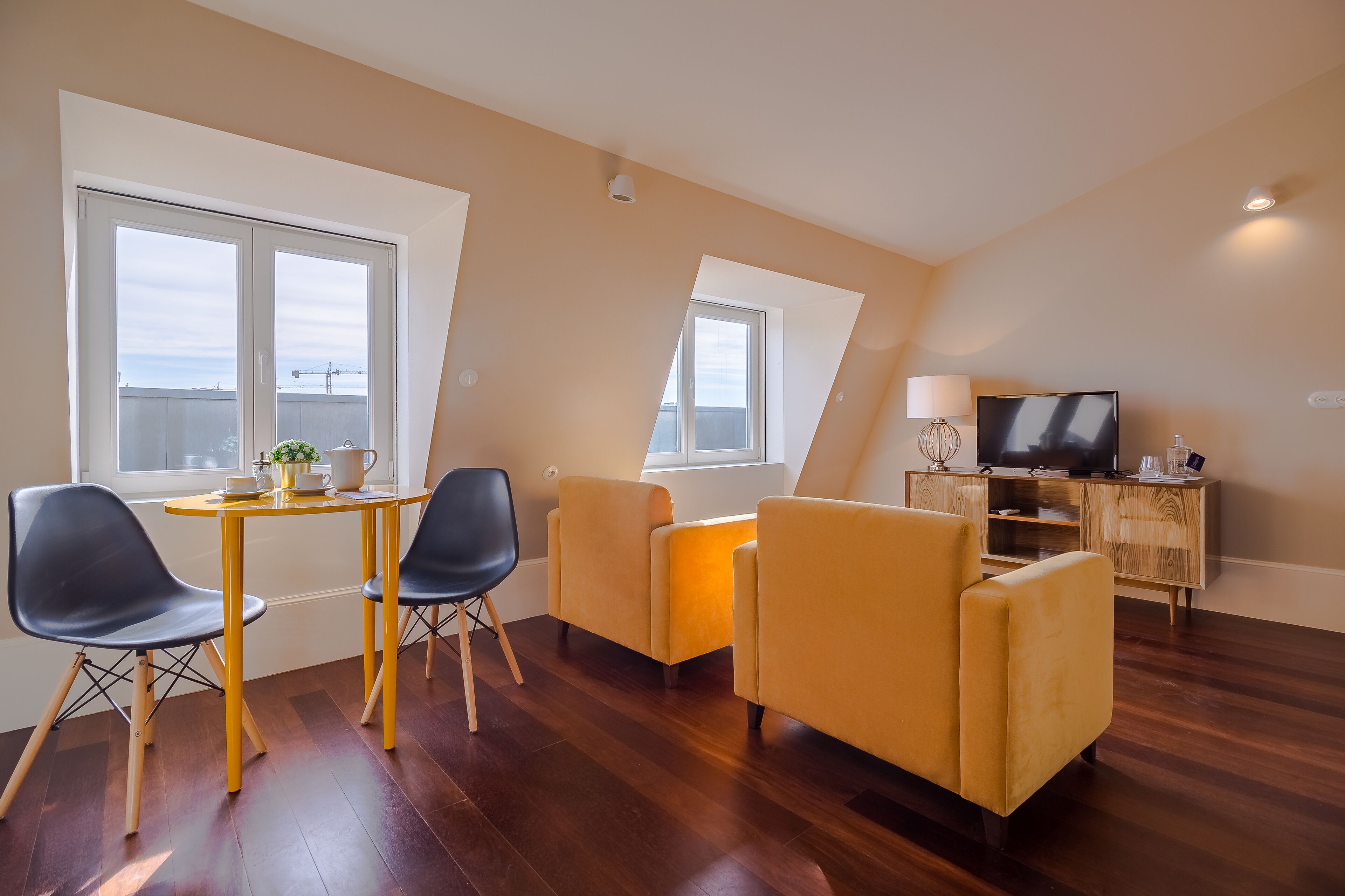 A modern living room with a wooden floor, a dining table with chairs, a sofa, a TV, and a lamp.
