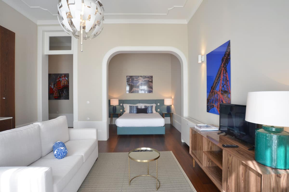 A modern hotel room with a large bed, a sofa, a television, and a desk.