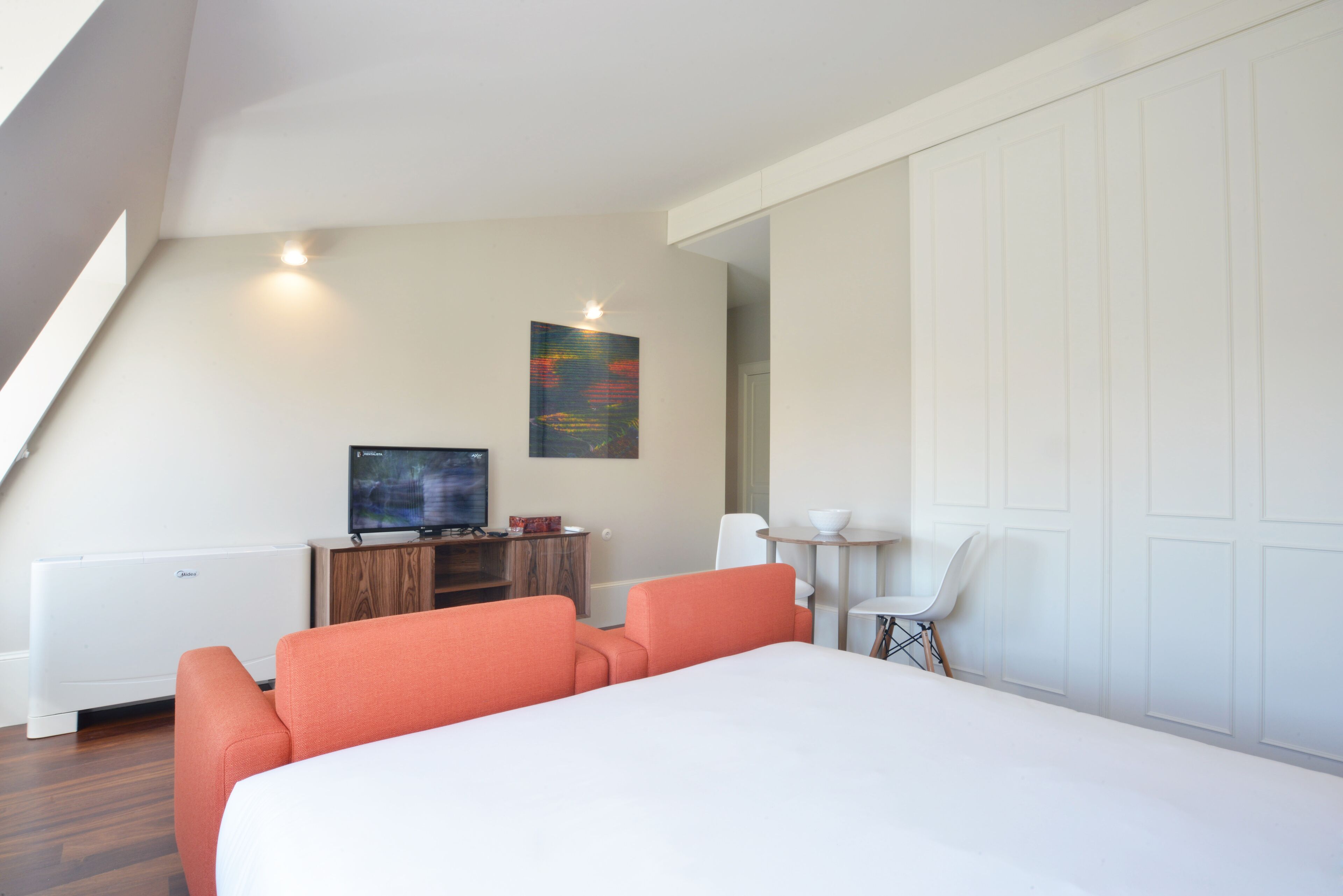 A modern hotel room with a large bed, a television, a small table, and a white chair.
