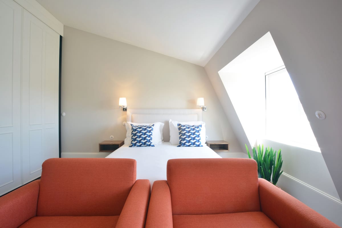 A bedroom with a bed, two nightstands, two lamps, and a window with a plant.