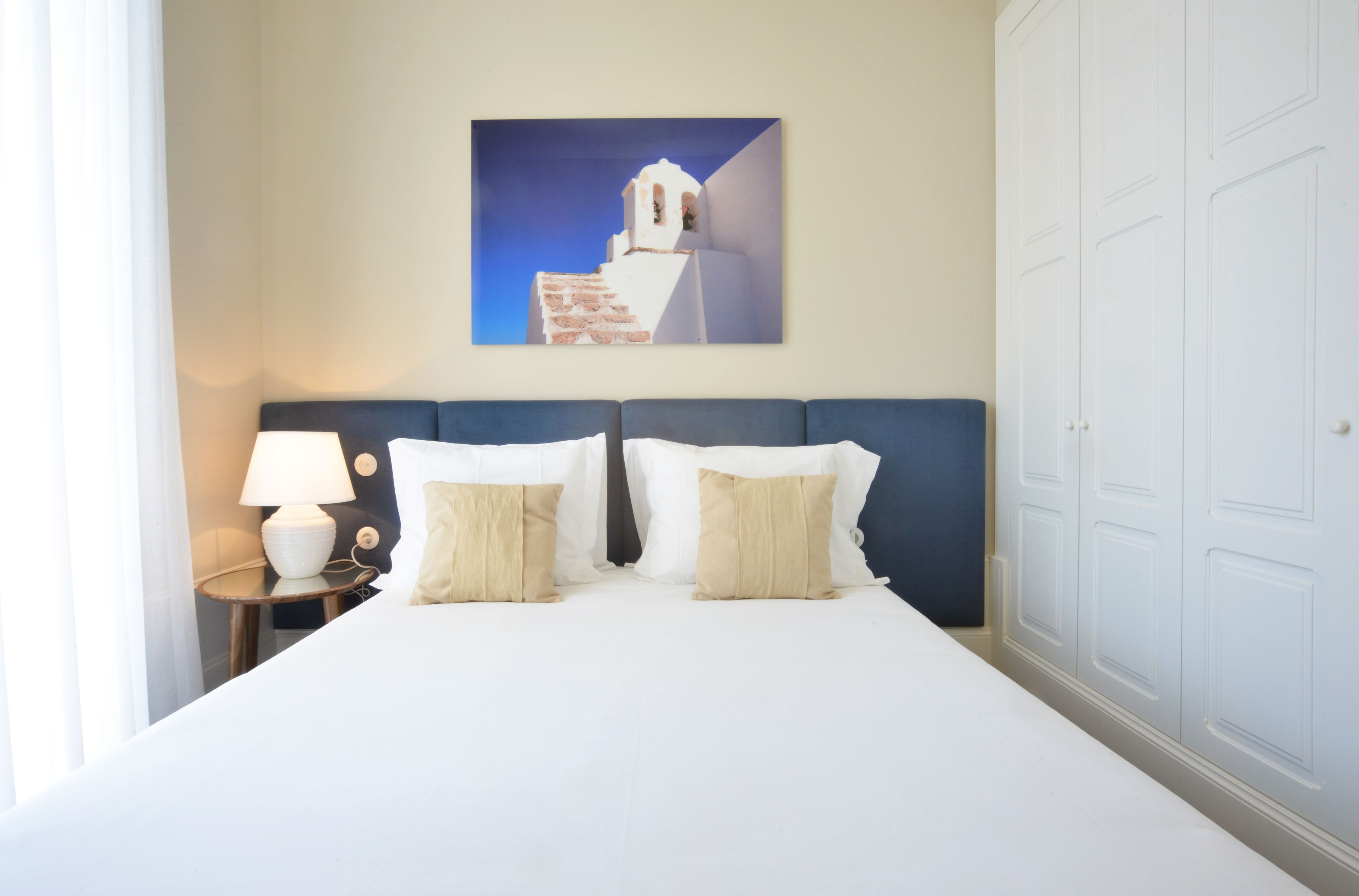 Una habitación de hotel con una cama, dos mesitas de noche, una lámpara y un cuadro colgado en la pared de un edificio.