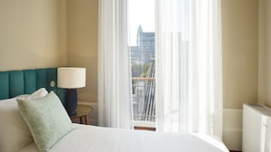A hotel room with a bed, a lamp, a view of buildings through sheer curtains, and a radiator. - YOUROPO - Market (Porto)